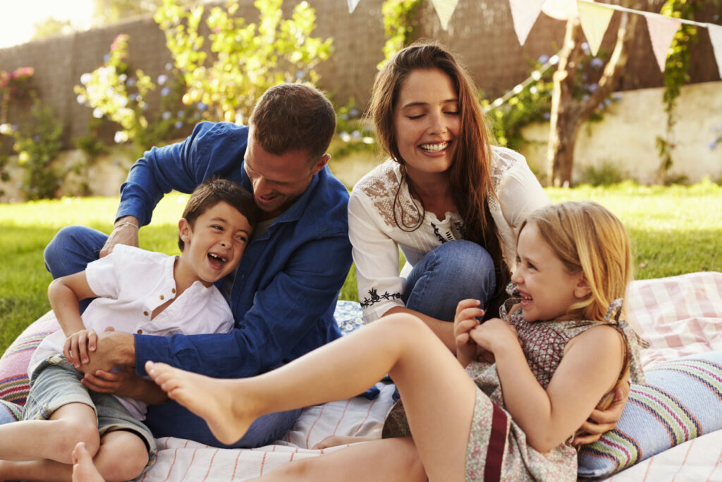 Parents Playing Game With Children On Blanket In Garden